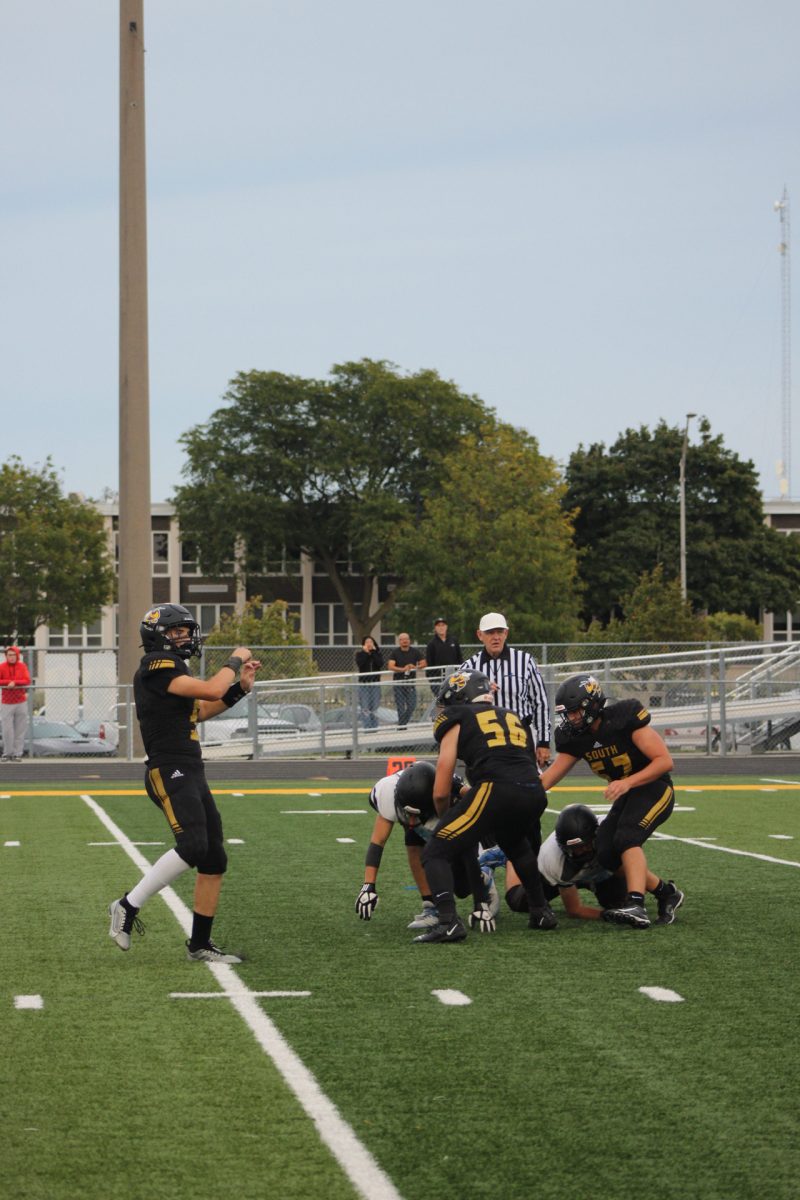 The junior varsity quarterback throwing the ball as the offensive line tries to stop the incoming defensive line trying to tackle and take the ball from the quarterback.